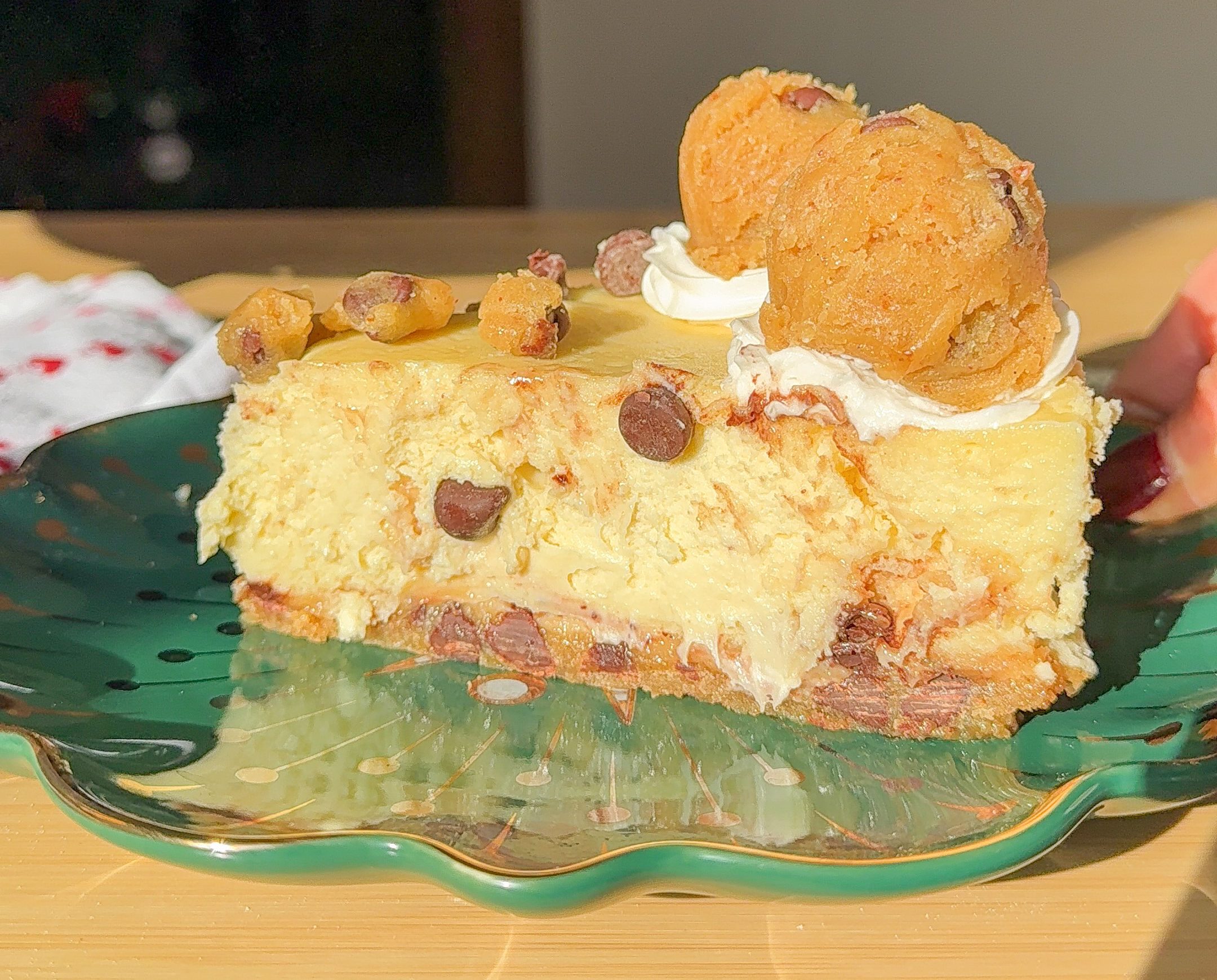 a slice of chocolate chip cookie cheesecake on a green plate and wood table.