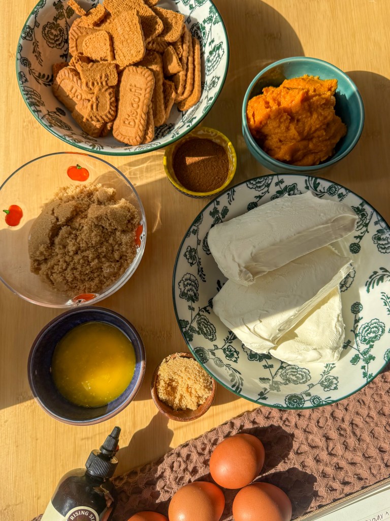 Ingredients for pumpkin cheesecake including Biscoff cookies, cream cheese, pumpkin puree, brown sugar, eggs, and pumpkin pie spice