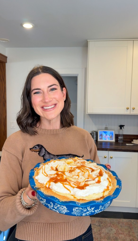 Mallory holding a banana pudding pie topped with whipped cream, banana slices, crushed vanilla wafers, and salted caramel